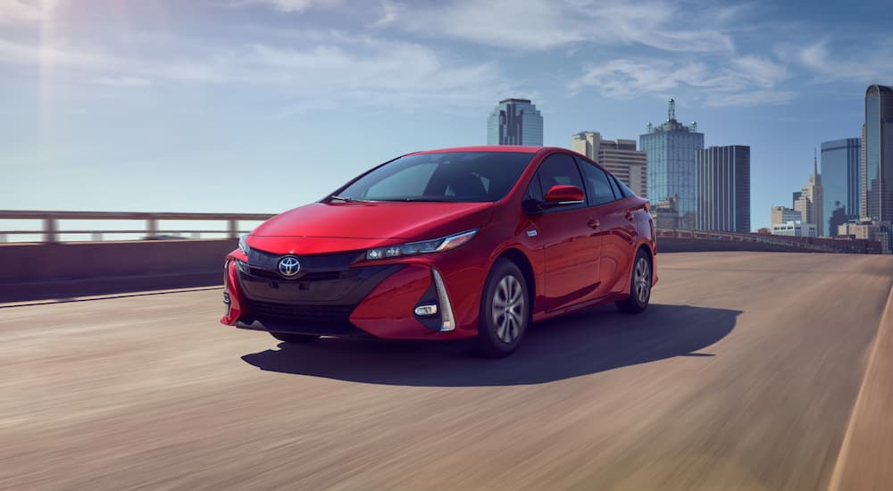 A red 2021 Toyota Prius Prime is driving on a highway away from a city.