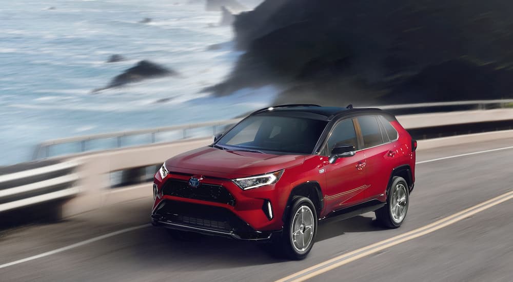 A red 2021 Toyota RAV4 Prime, which is new for the 2021 Toyota Hybrids, is driving past the ocean.