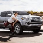 A person is skateboarding by a silver 2021 Toyota Tacoma.