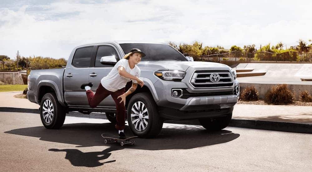 A person is skateboarding by a silver 2021 Toyota Tacoma.