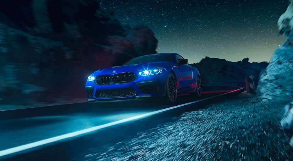 A popular BMW sports car, a blue 2021 BMW M8 coupe, is driving down the road at night.