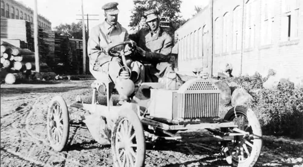 A 1904 Buick Model B Touring is shown in black and white parked in lumber yard.