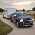 A black 2016 used Chevy Silverado 1500 is towing a horse trailer out of a driveway.