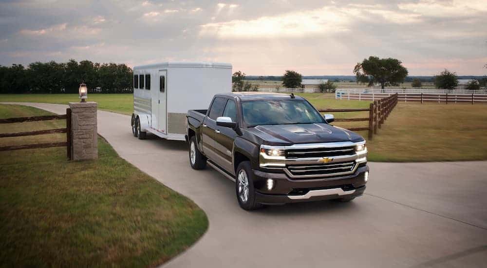 A black 2016 used Chevy Silverado 1500 is towing a horse trailer out of a driveway.