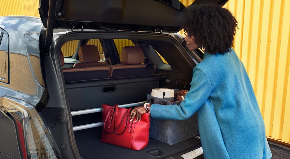 A woman is moving bags in the back of her 2020 Cadillac XT5 that is parked in front of a yellow wall.
