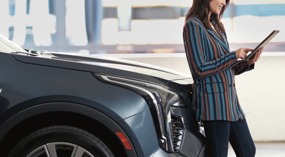 A woman is leaning on a grey Cadillac SUV while ordering from Amazon on a tablet.