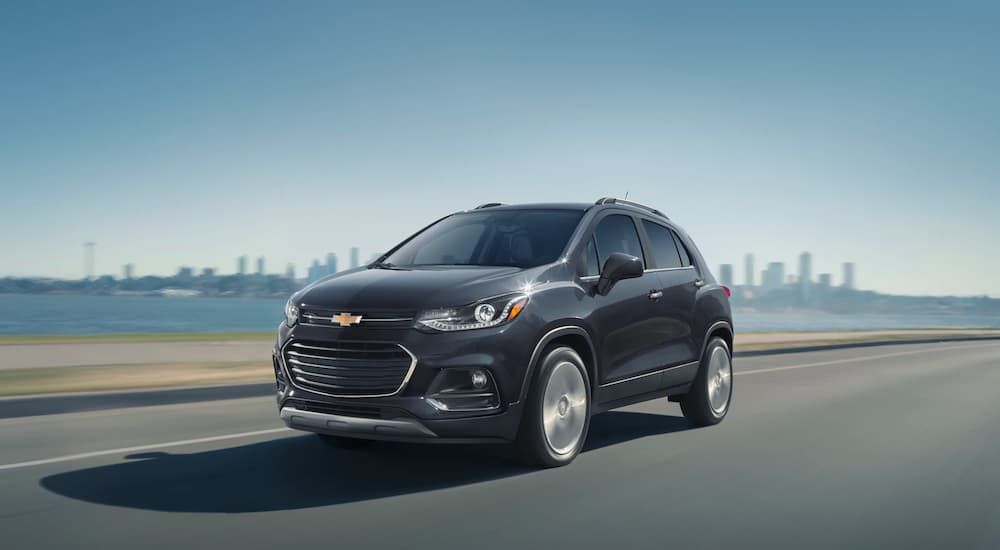 A black 2020 Chevy Trax is dirving down the road away from a city.