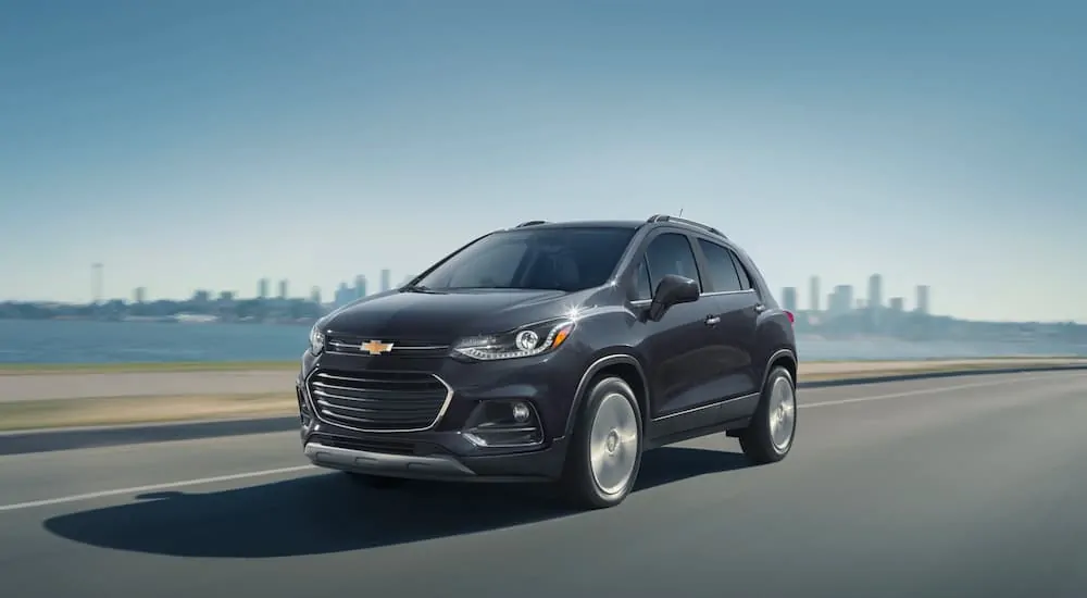 A black 2020 Chevy Trax is dirving down the road away from a city.