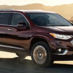 A burgundy 2021 Chevy Traverse is driving on a desert road at sunset.