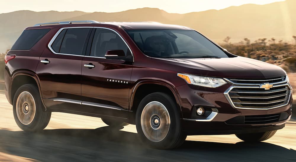 A burgundy 2021 Chevy Traverse is driving on a desert road at sunset.