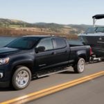 A black 2021 Chevy Colorado, the smallest Chevy diesel truck, is towing a boat past a lake.