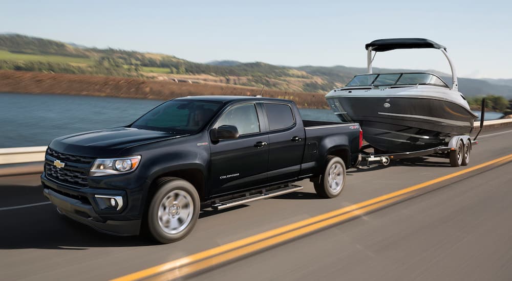 A black 2021 Chevy Colorado, the smallest Chevy diesel truck, is towing a boat past a lake.