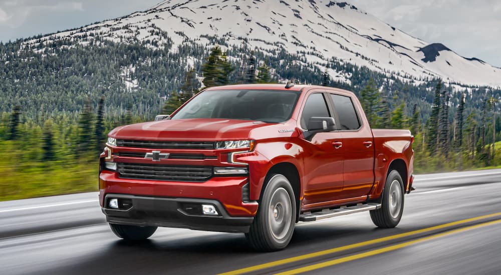 A red 2021 Chevy Silverado 1500 is driving past a snowy mountain.