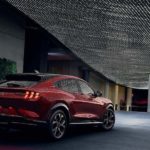 A red 2021 Ford Mustang Mach-E is parked under many lights reflected off of the vehicle.