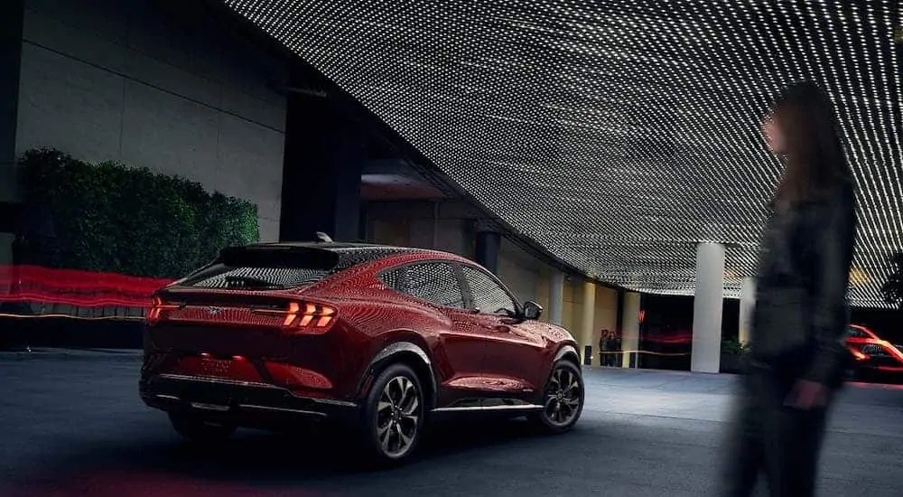 A red 2021 Ford Mustang Mach-E is parked under many lights reflected off of the vehicle.