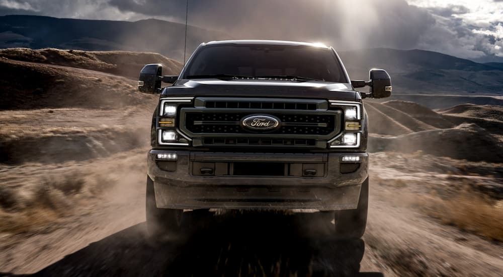 A black 2021 Ford diesel truck, a black Super Duty, is shown from the front driving on a dirt path with distant mountains.