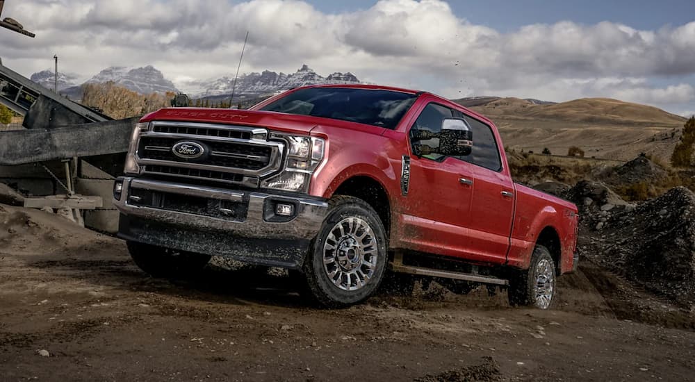 A red 2021 Ford F-250 is off-roading on dirt in front of distant snowy mountains.