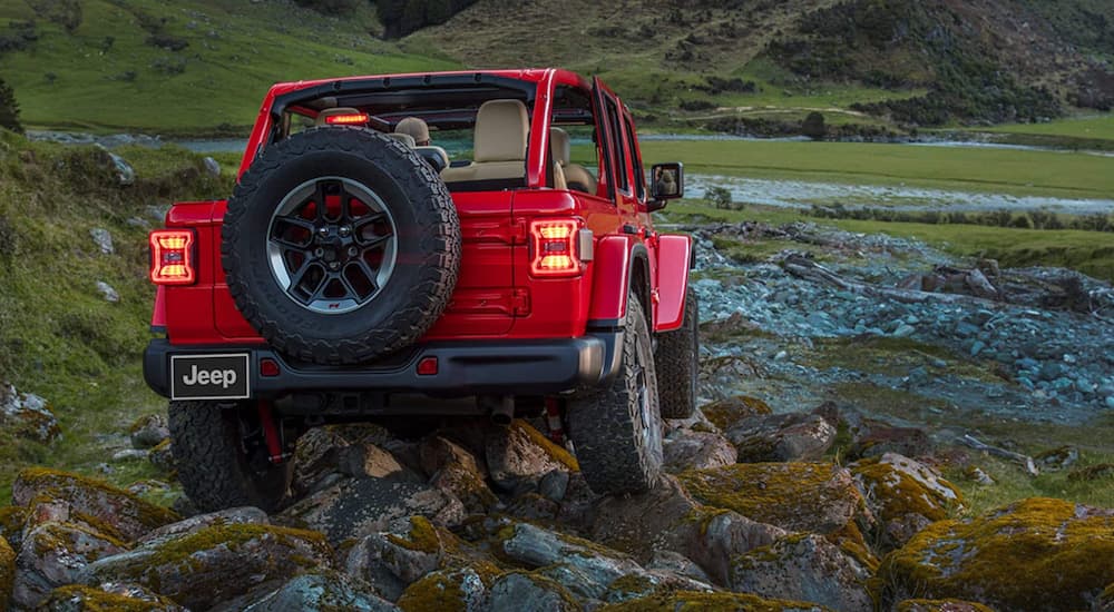 A red 2021 Jeep Wrangler Unlimited is shown from the rear off-roading on rocks down to a river after leaving a Jeep Wrangler dealer near Lexington.