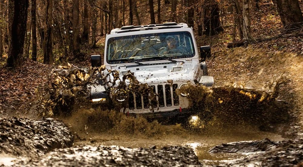 A white 2021 Jeep Wrangler Rubicon is off-roading in the mud.