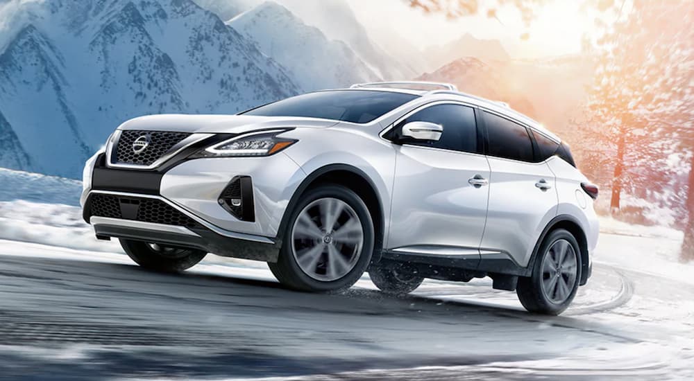 A white 2021 Nissan Murano from a Nissan dealer is driving around a corner on a snowy mountain road.