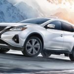 A white 2021 Nissan Murano is driving around a corner on a snowy mountain road.