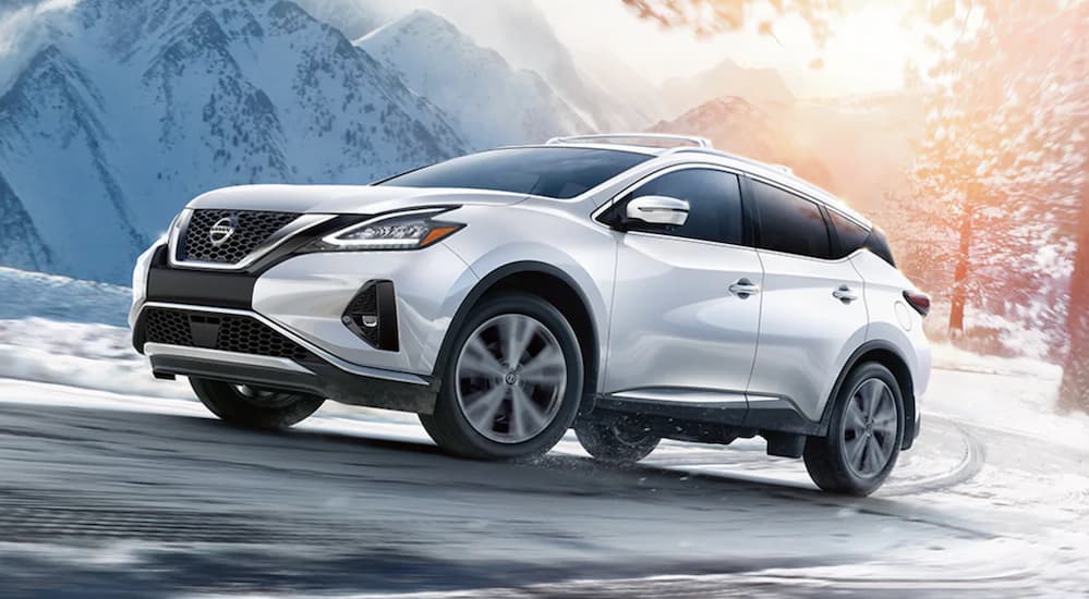 A white 2021 Nissan Murano is driving around a corner on a snowy mountain road.