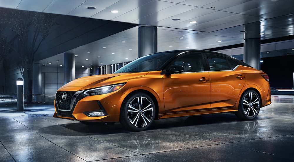 An orange 2021 Nissan Sentra is parked at a modern Nissan dealer at night.