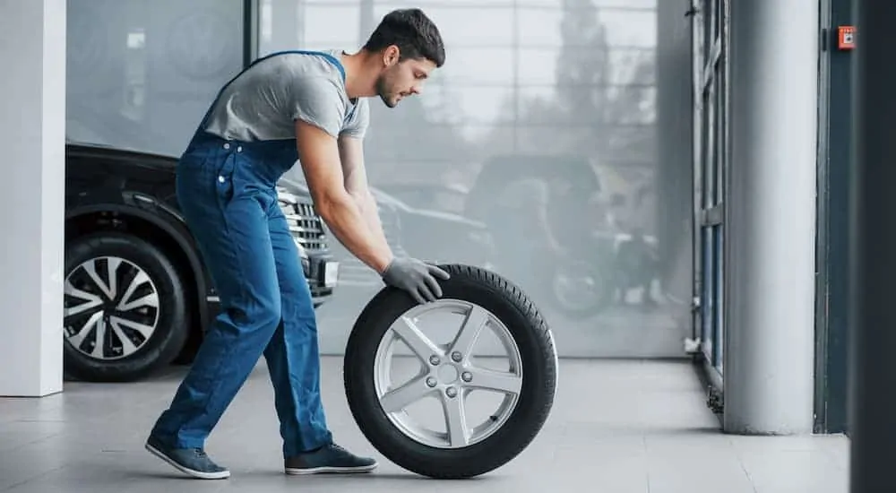 A mechanic is rolling a tire and rim in a workshop.