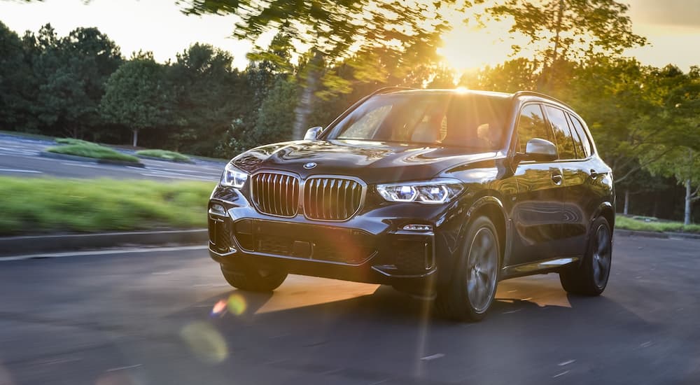 A black 2018 Used BMW X5 is driving through a parking lot with trees and sunshine.