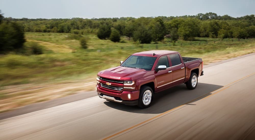 A red 2018 Chevy Silverado is shown from a higher angle driving past grass and trees after leaving a dealership for used cars in Durham, NC.