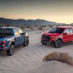 A blue and a red 2019 used Ford F-150 Raptor are parked in the sand dunes.