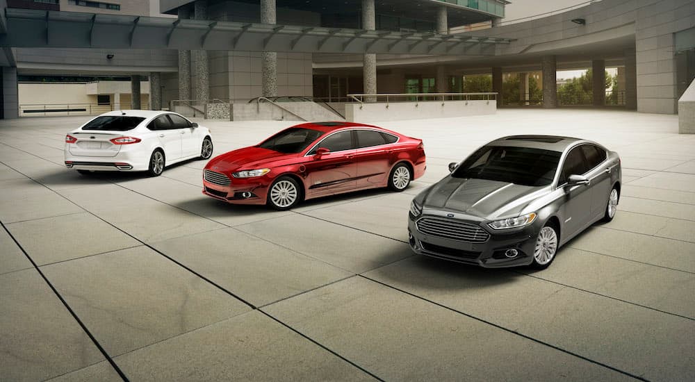 A white, a red, and a grey 2015 used Ford Fusion are parked in a concrete courtyard.