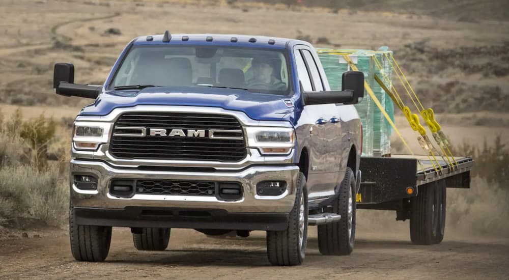 A blue 2019 Ram 2500 is towing building material on a desert road.