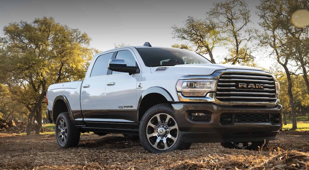 A white 2020 used Ram 2500 is parked off-road in front of trees.