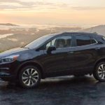 A black 2021 Buick Encore is parked at a lookout in front of mountains at sunset.