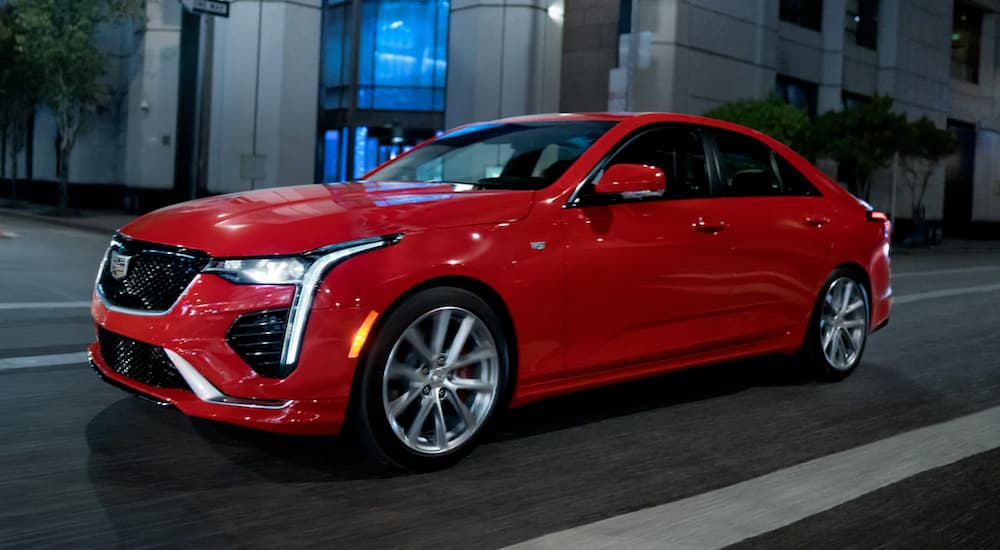 A red 2021 Cadillac CT4 is driving on a city street at night.