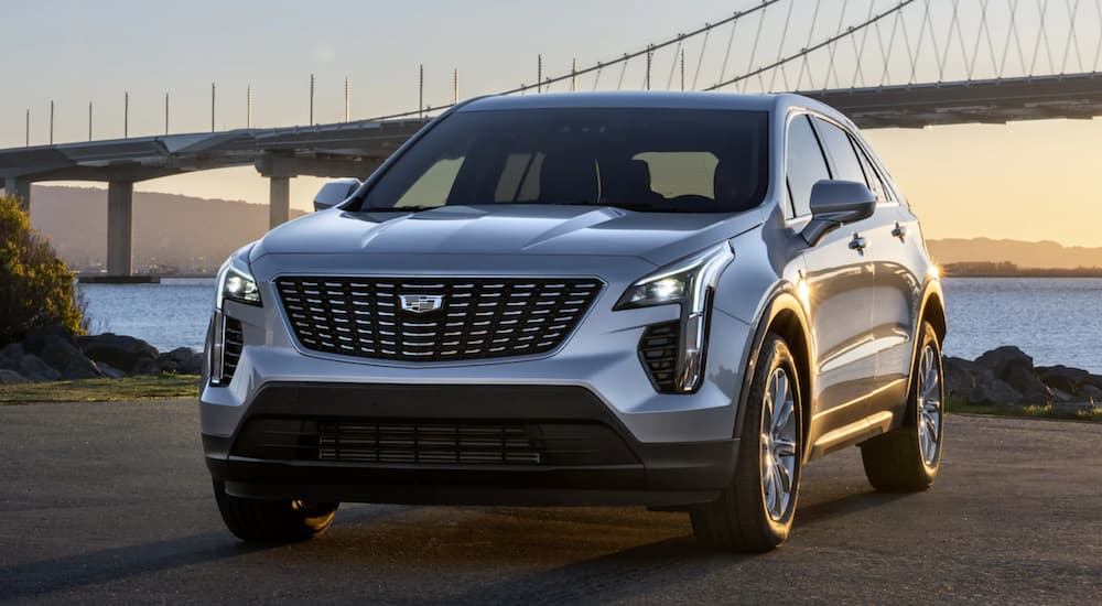 A silver 2021 Cadillac XT4 is parked in front of a bay and bridge at sunset.