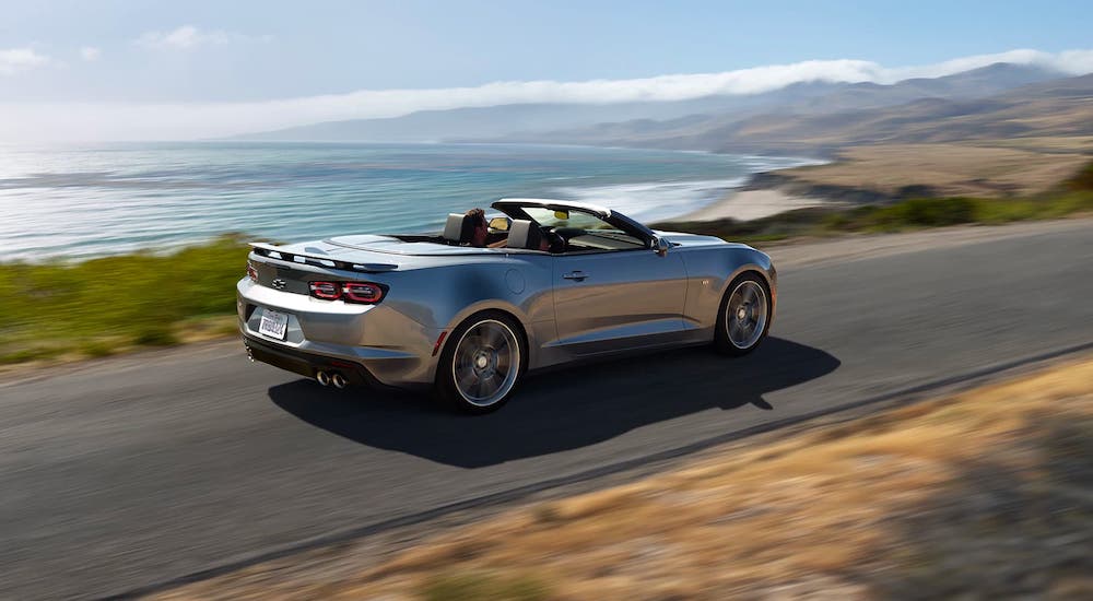 silver 2021 Chevy Camaro Convertible is driving on a coastal highway after the 2021 Chevy Camaro vs 2021 Ford Mustang comaprison.