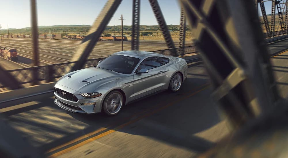 A silver 2021 Ford Mustang is driving over a bridge.