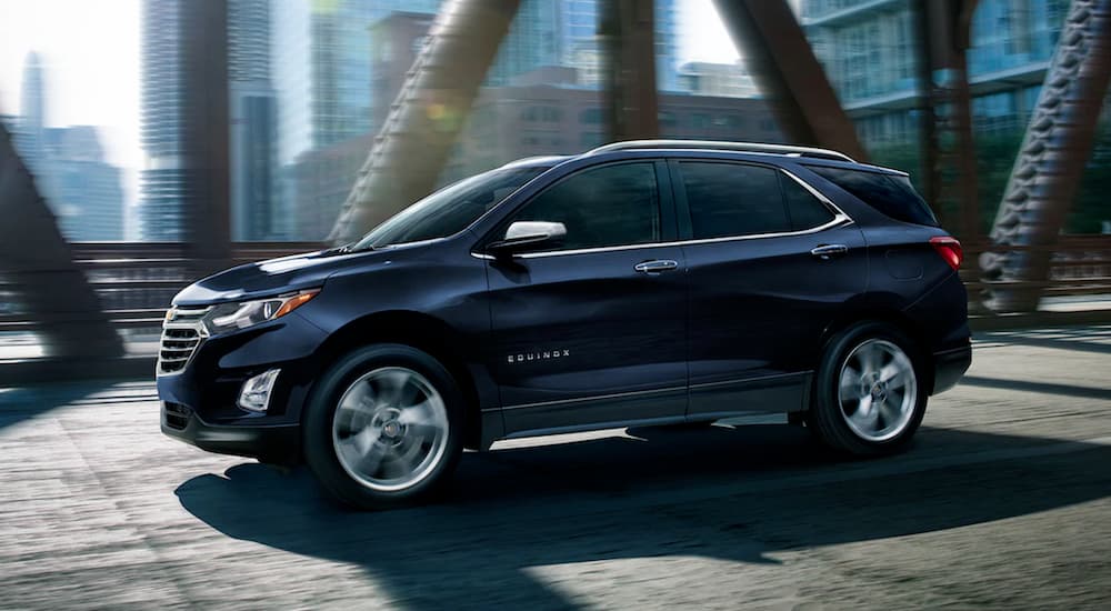 A blue 2021 Chevy Equinox is driving on a city bridge.