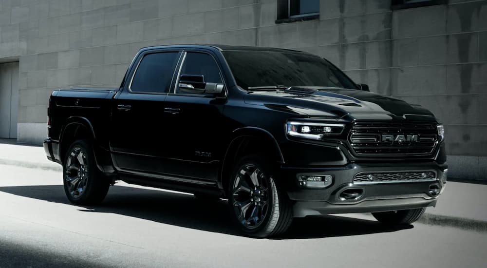 A black 2021 Ram 1500 is driving past a grey building.