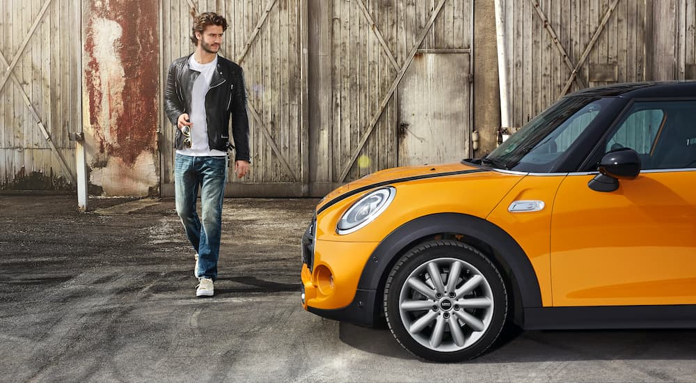 A man is shown approaching an orange 2015 Mini Cooper S parked outside of a barn.