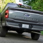 A grey 2021 Ford F-150 Hybrid is shown from the rear on a tree-lined road.