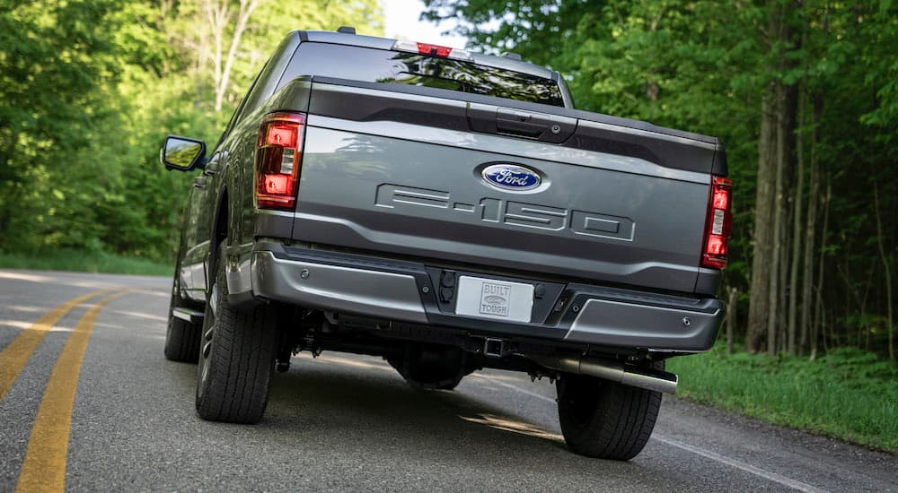 A grey 2021 Ford F-150 Hybrid is shown from the rear on a tree-lined road.