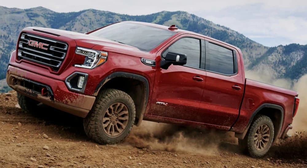 A red 2021 GMC Sierra 1500 AT4 is off-roading on dirt with mountains behind it.