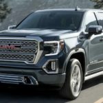 A grey 2021 GMC Sierra 1500 is driving on a mountain road past a guard rail and pine trees.