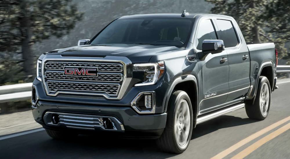 A grey 2021 GMC Sierra 1500 is driving on a mountain road past a guard rail and pine trees.