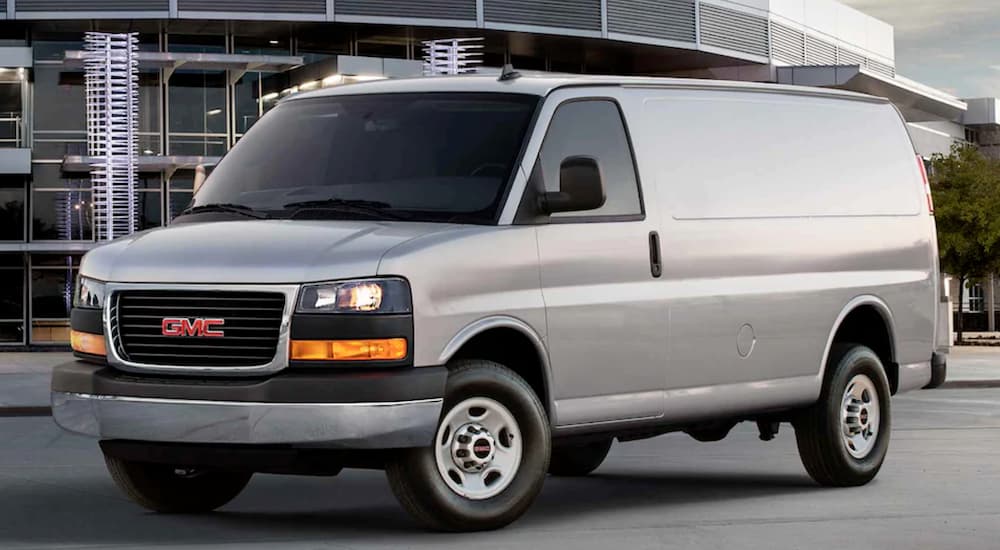 A grey 2021 GMC Work Van Savana is shown from the side in front of a modern building.