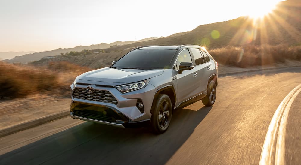 A grey 2021 Toyota RAV4 is driving around a corner with the sun shining over a hill.