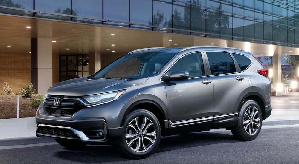 A grey 2021 Honda CR-V is parked in front of a glass building after winning the 2021 Honda CR-V vs 2021 Toyota RAV4 comparison.